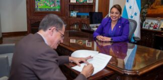 A man signs a paper as Honduran President Xiomara Castro watches from across the table