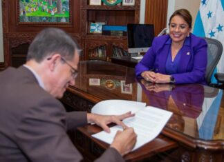 A man signs a paper as Honduran President Xiomara Castro watches from across the table