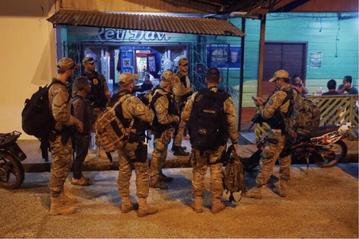 Armed personnel in camouflage and tactical vests gather outside buildings on a street at night.