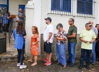 Voters queue beside the entrance to Escola Municipal Barão Homem de Mello in Rio de Janeiro, while an election worker directs people into the building.