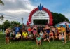 Brazil: When electricity is not enough Residents of the Nova Esperança Indigenous community pose beneath a red and blue welcome arch, surrounded by greenery and community buildings.